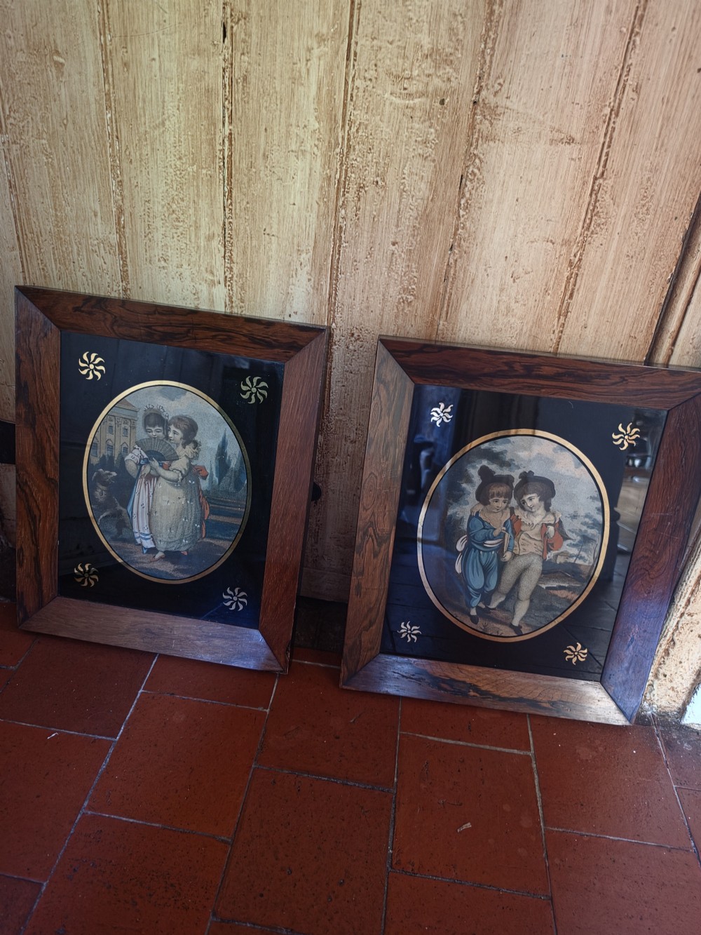 A pair of square rosewood picture frames featuring oval 19th-century prints of children set within black reverse-painted glass mounts with gold motifs. View VII