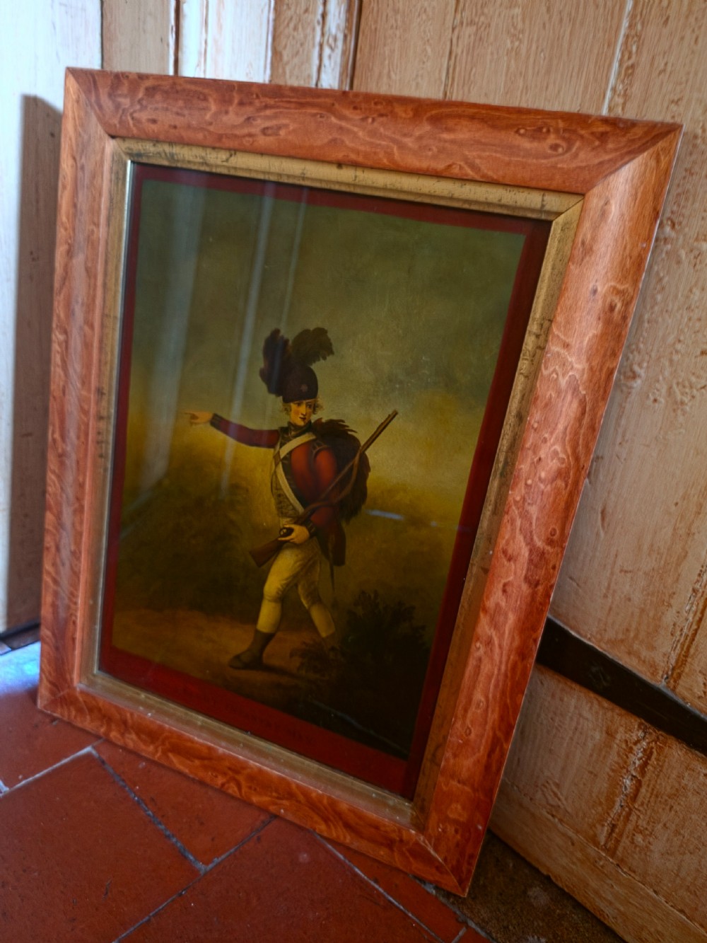 A 19th-century reverse glass picture depicting a Light Infantryman in a red coat, framed within a birds eye maple timber frame with a gilded inner slip.