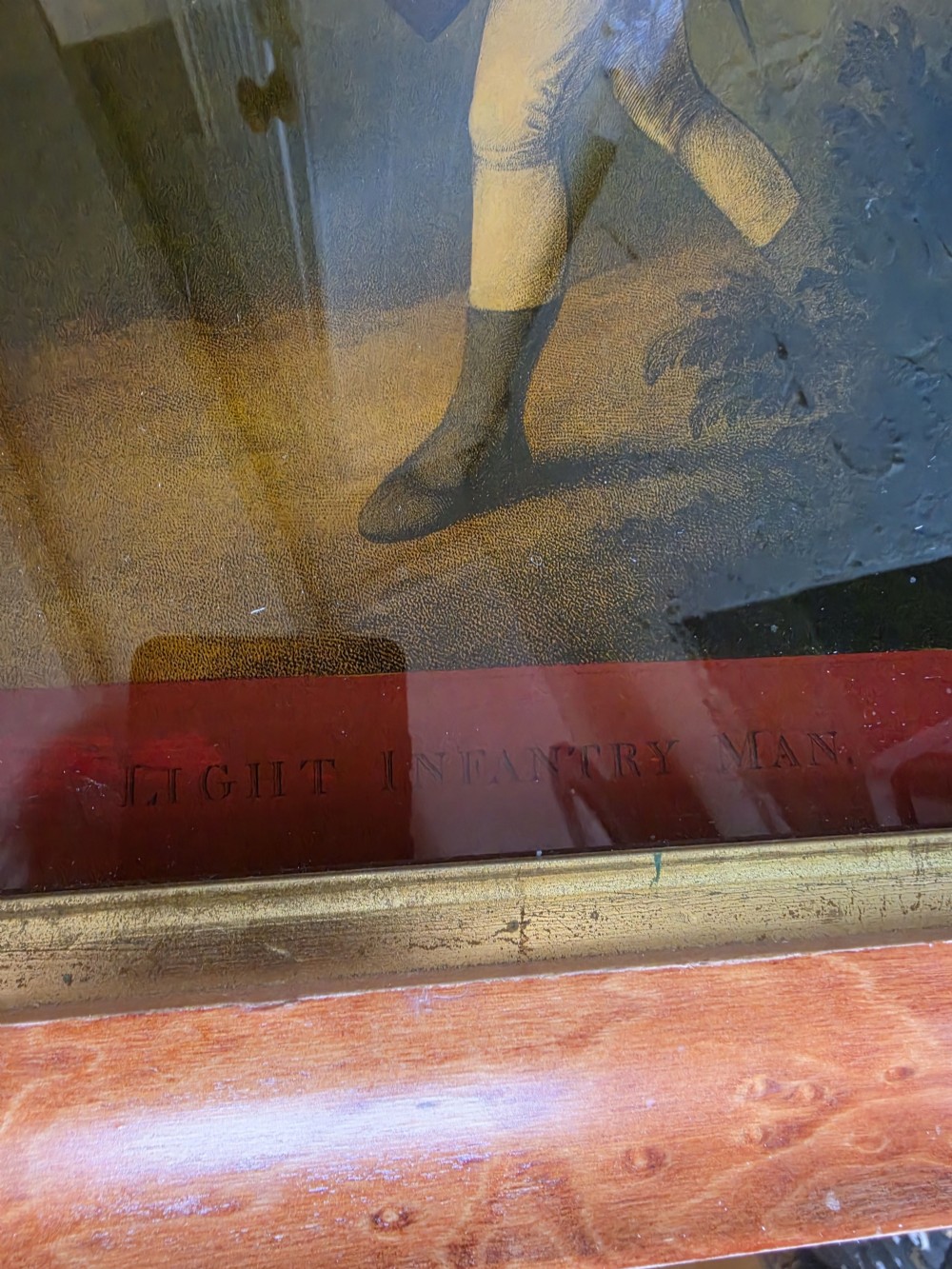 A 19th-century reverse glass picture depicting a Light Infantryman in a red coat, framed within a birds eye maple timber frame with a gilded inner slip. View III
