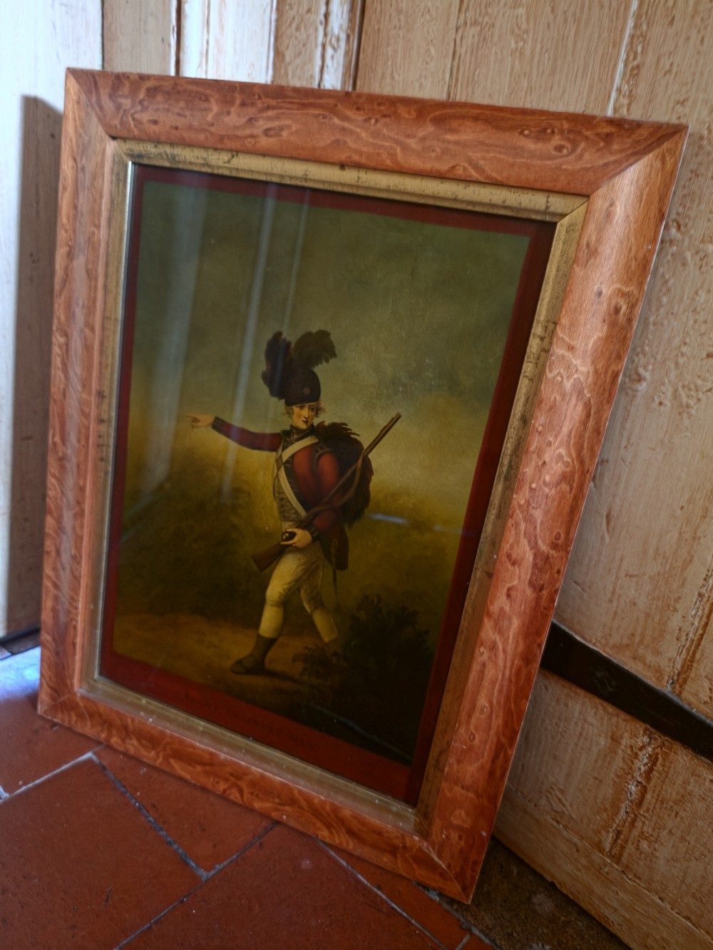A 19th-century reverse glass picture depicting a Light Infantryman in a red coat, framed within a birds eye maple timber frame with a gilded inner slip. View V