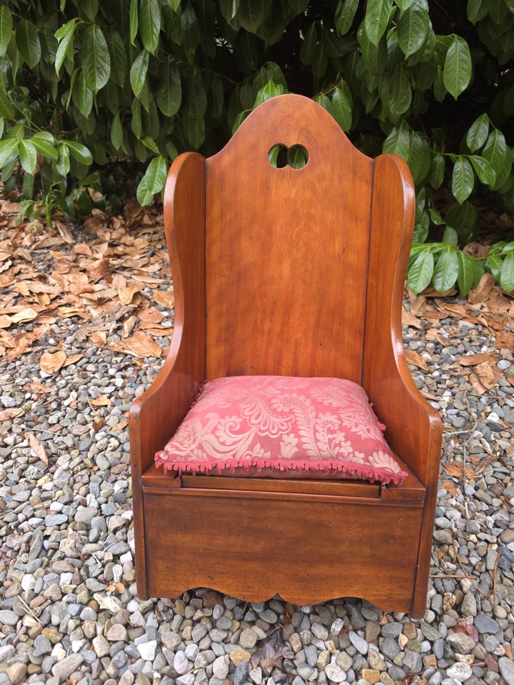 A Georgian fruitwood childs potty chair featuring high winged sides, a cutout motif on the top backrest, a hinged wooden seat, and integrated rocker bases. View II
