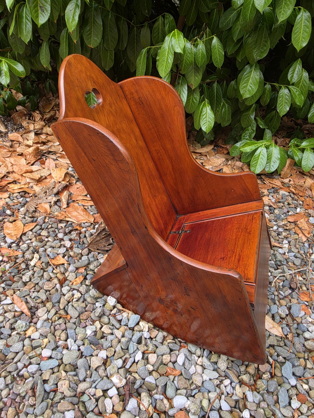 A Georgian fruitwood childs potty chair featuring high winged sides, a cutout motif on the top backrest, a hinged wooden seat, and integrated rocker bases. View V