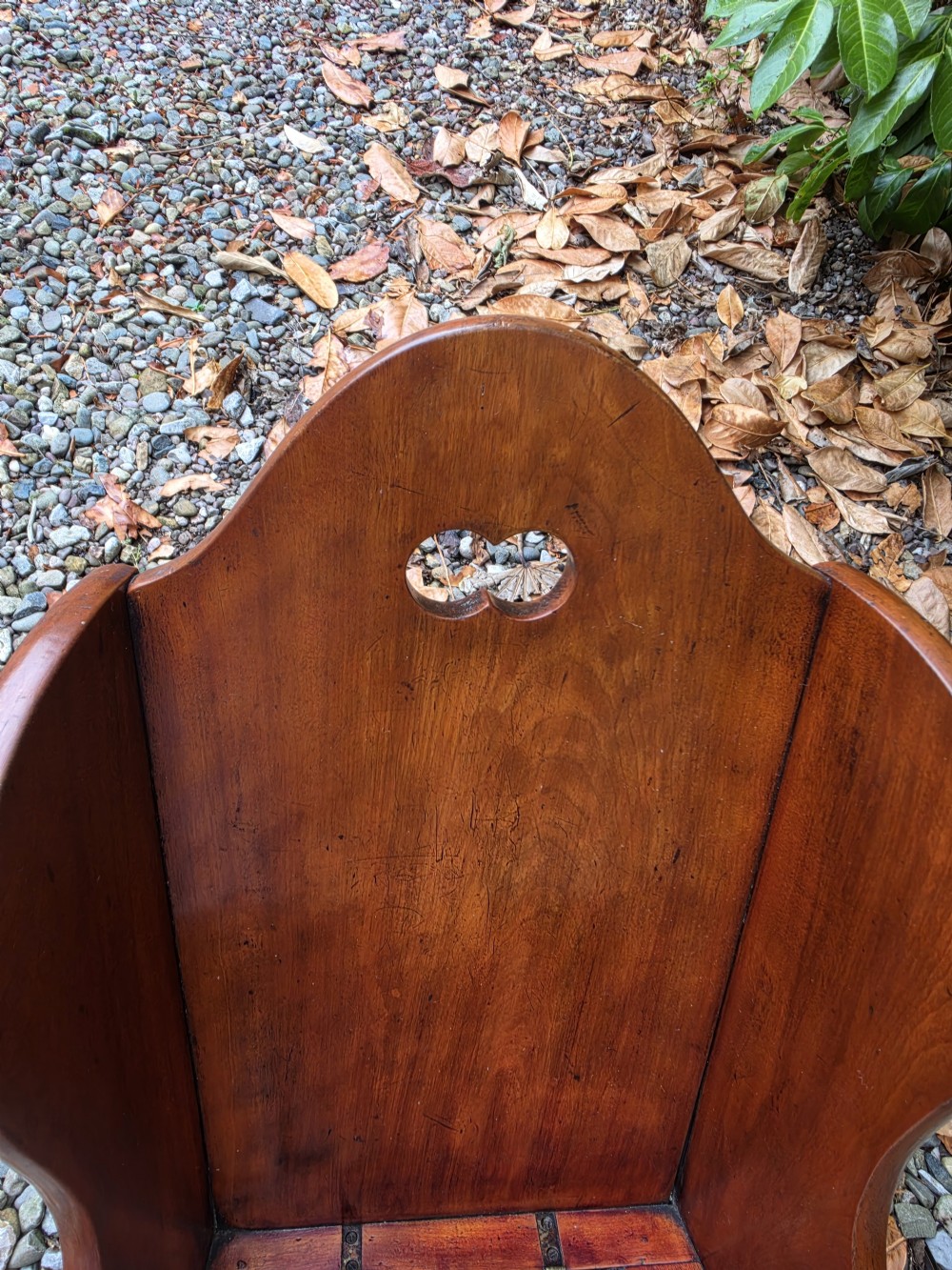 A Georgian fruitwood childs potty chair featuring high winged sides, a cutout motif on the top backrest, a hinged wooden seat, and integrated rocker bases. View VI