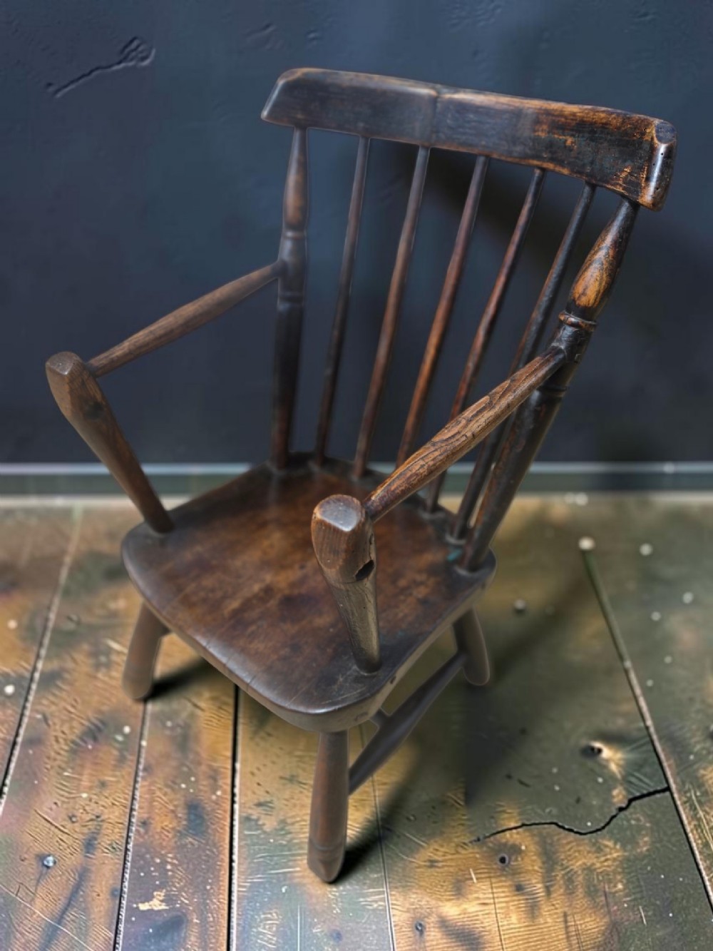 A 19th-century West Country childs Windsor armchair made of dark wood, featuring vertical back spindles, a shaped seat, and turned splayed legs.