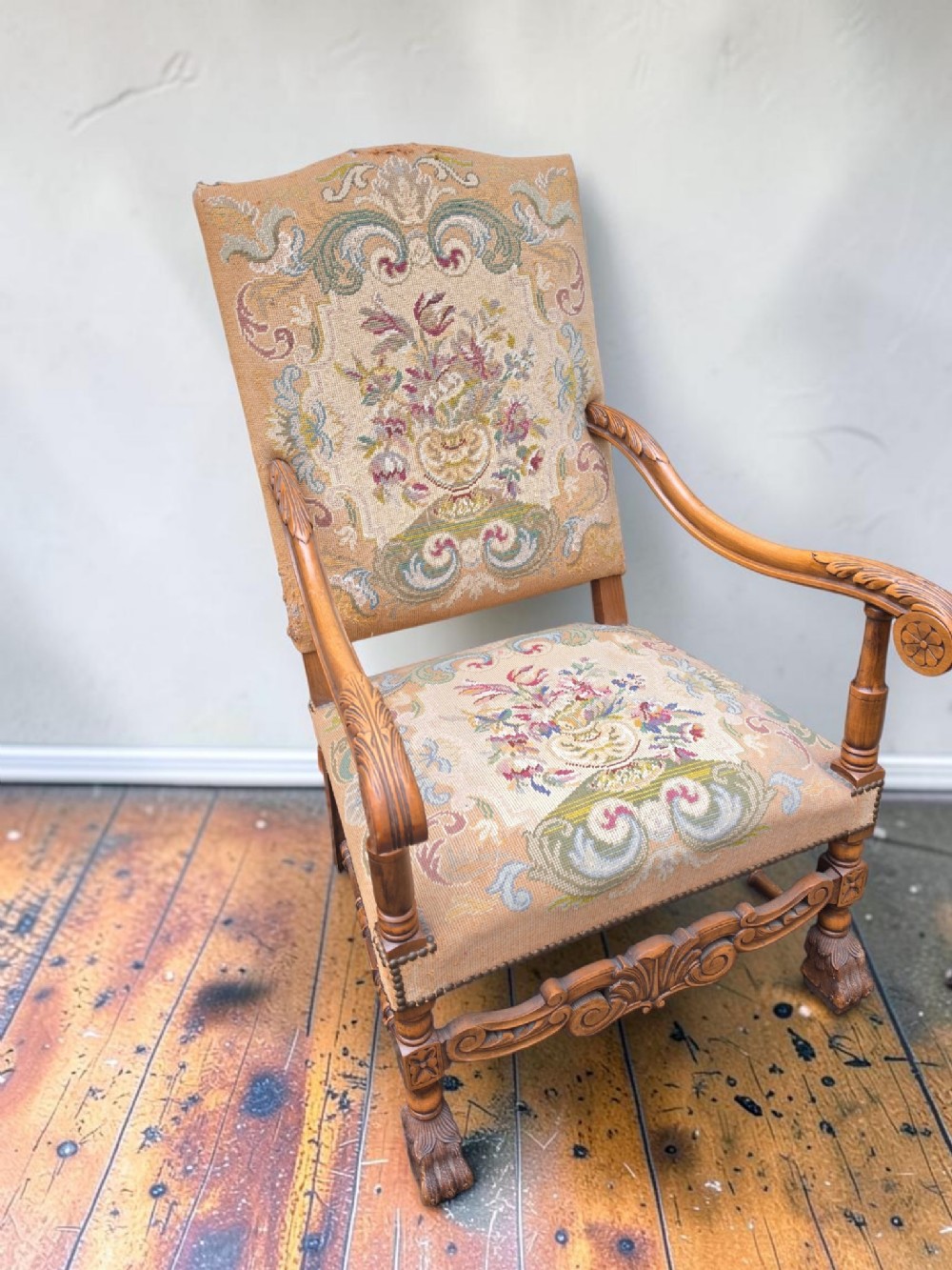 A 19th-century carved walnut armchair featuring scroll arms, turned legs, and floral needlepoint tapestry upholstery with brass stud trim.