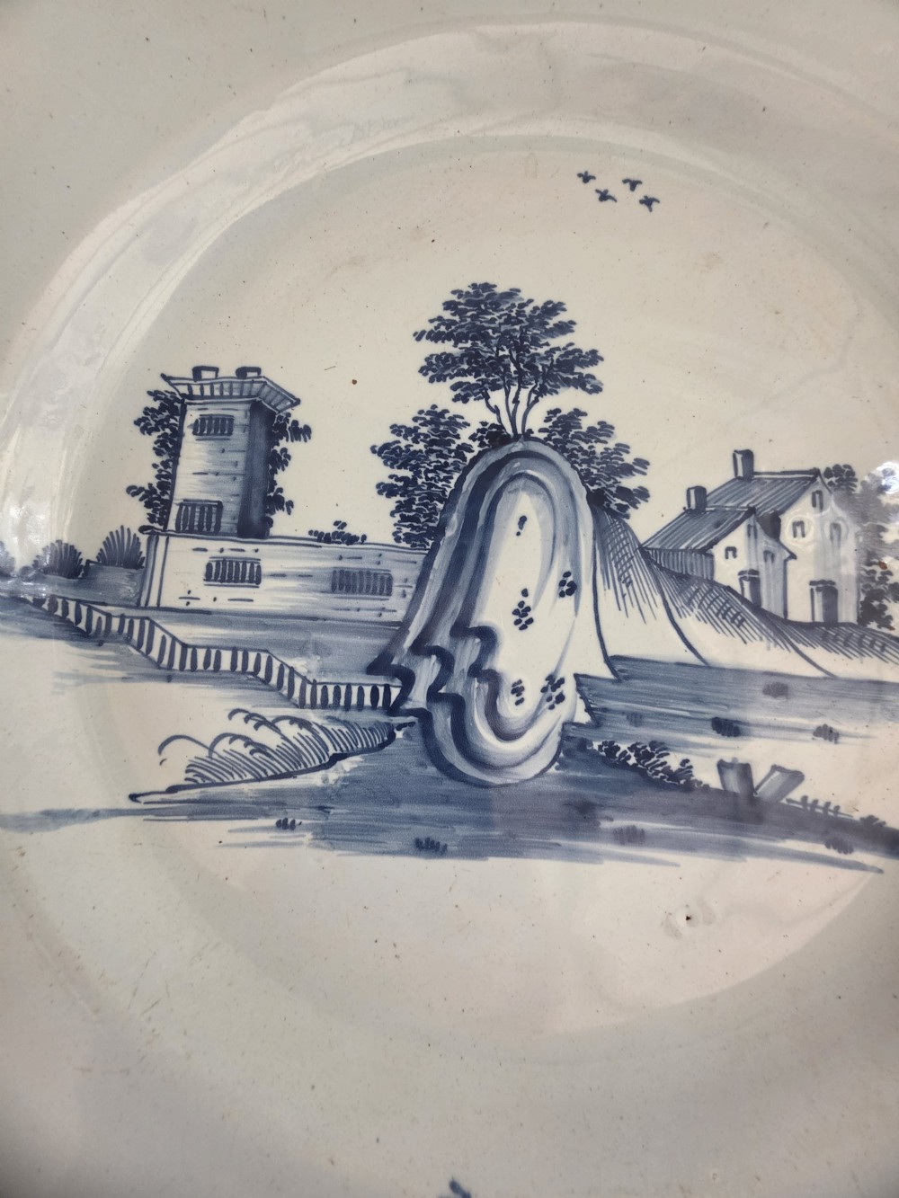An 18th-century circular Bristol delftware charger plate featuring a hand-painted blue landscape scene on a white tin-glazed surface. View V