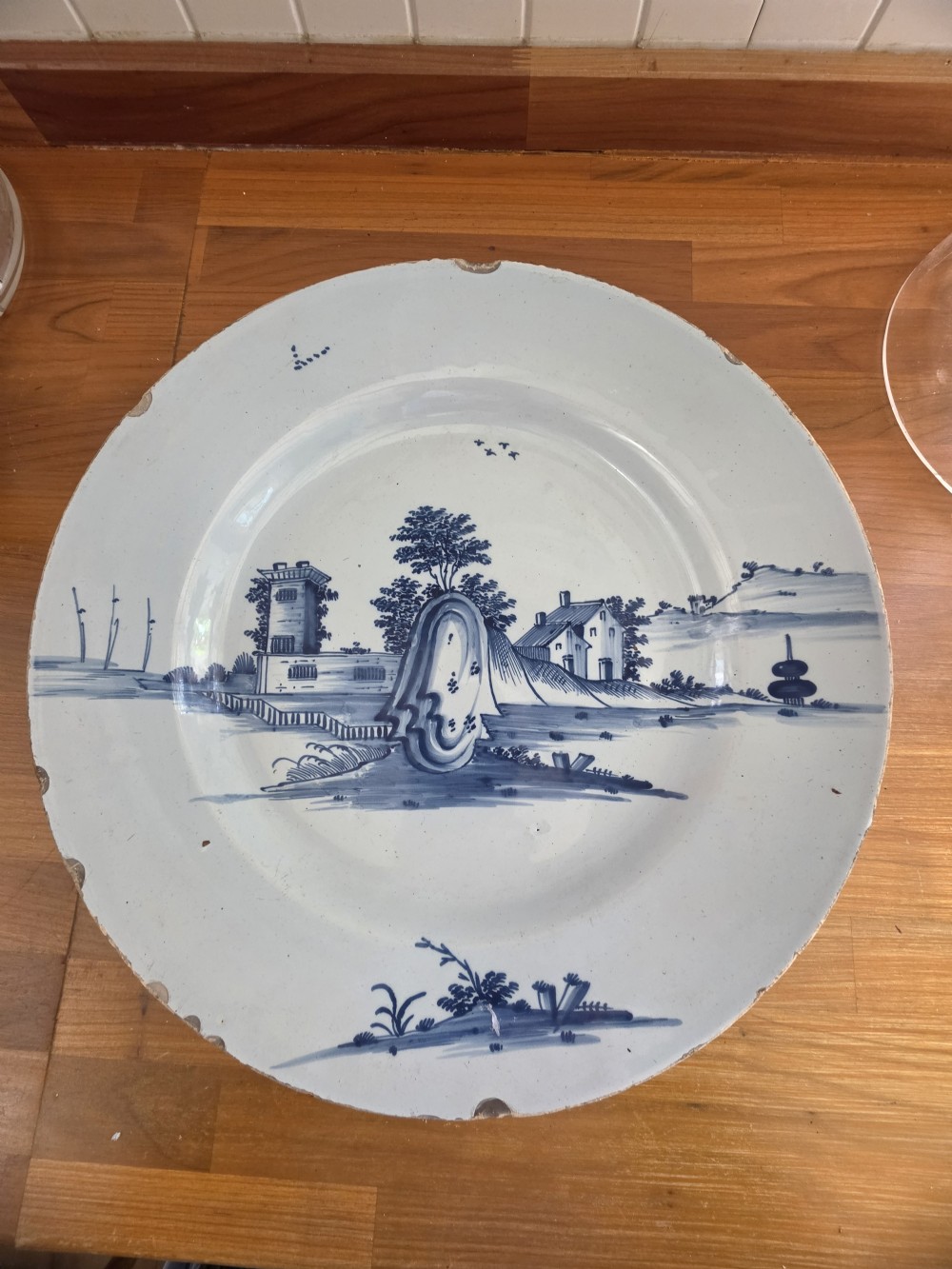 An 18th-century circular Bristol delftware charger plate featuring a hand-painted blue landscape scene on a white tin-glazed surface. View VII