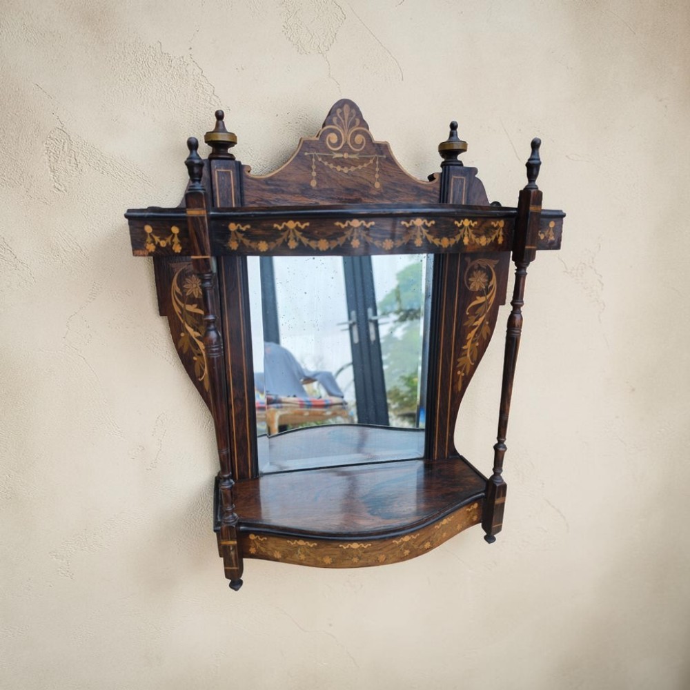 A dark mahogany wall mirror featuring light wood floral inlay, turned side columns, a shaped crest, and two integrated display shelves.