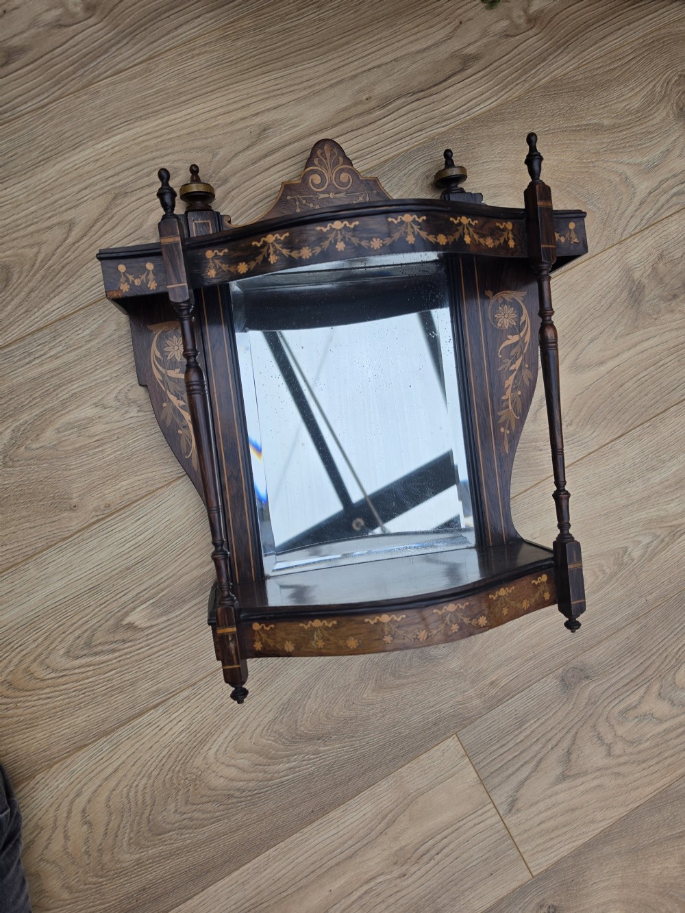 A dark mahogany wall mirror featuring light wood floral inlay, turned side columns, a shaped crest, and two integrated display shelves. View V