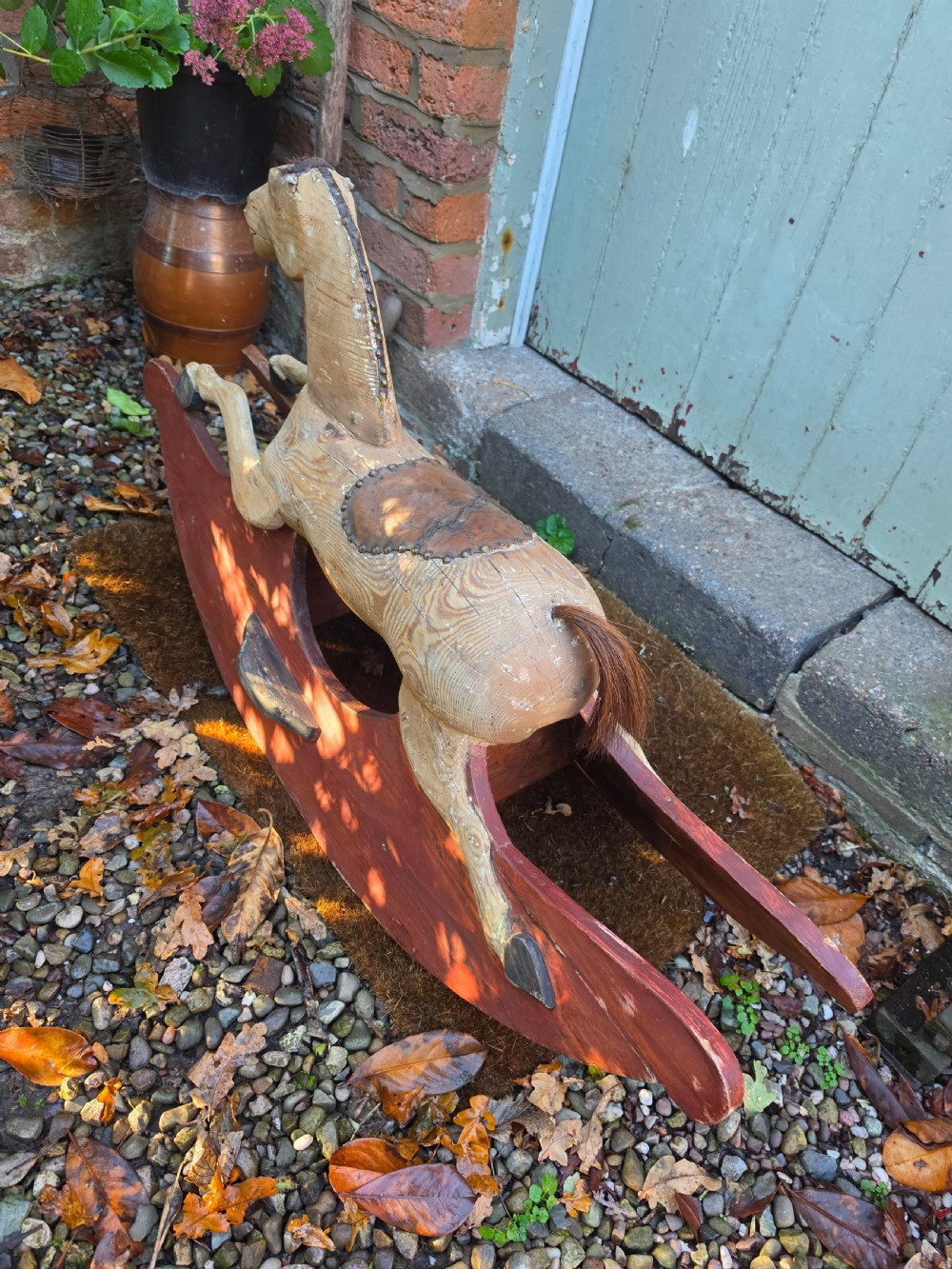 A 19th-century carved wooden rocking horse with visible grain, leather saddle detail, and a dark red painted bow rocker base. View II