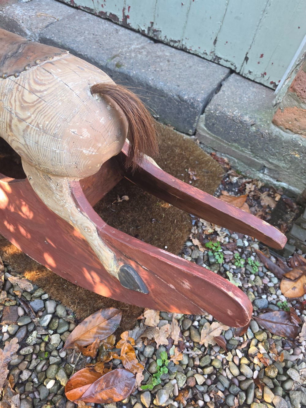 A 19th-century carved wooden rocking horse with visible grain, leather saddle detail, and a dark red painted bow rocker base. View III