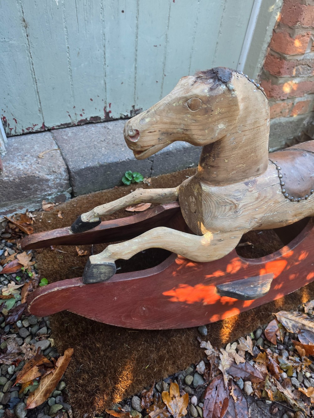 A 19th-century carved wooden rocking horse with visible grain, leather saddle detail, and a dark red painted bow rocker base. View IV