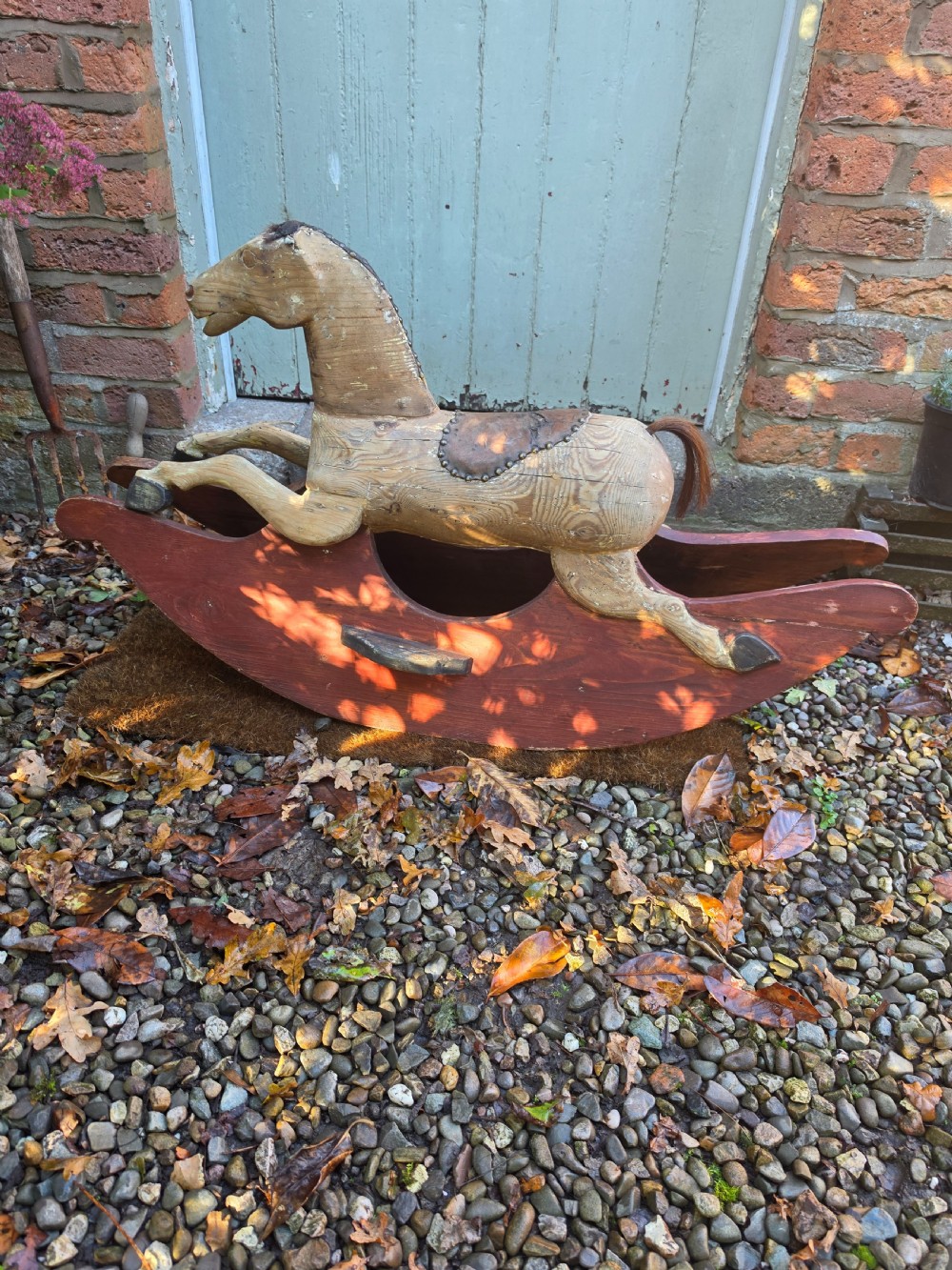 A 19th-century carved wooden rocking horse with visible grain, leather saddle detail, and a dark red painted bow rocker base. View V