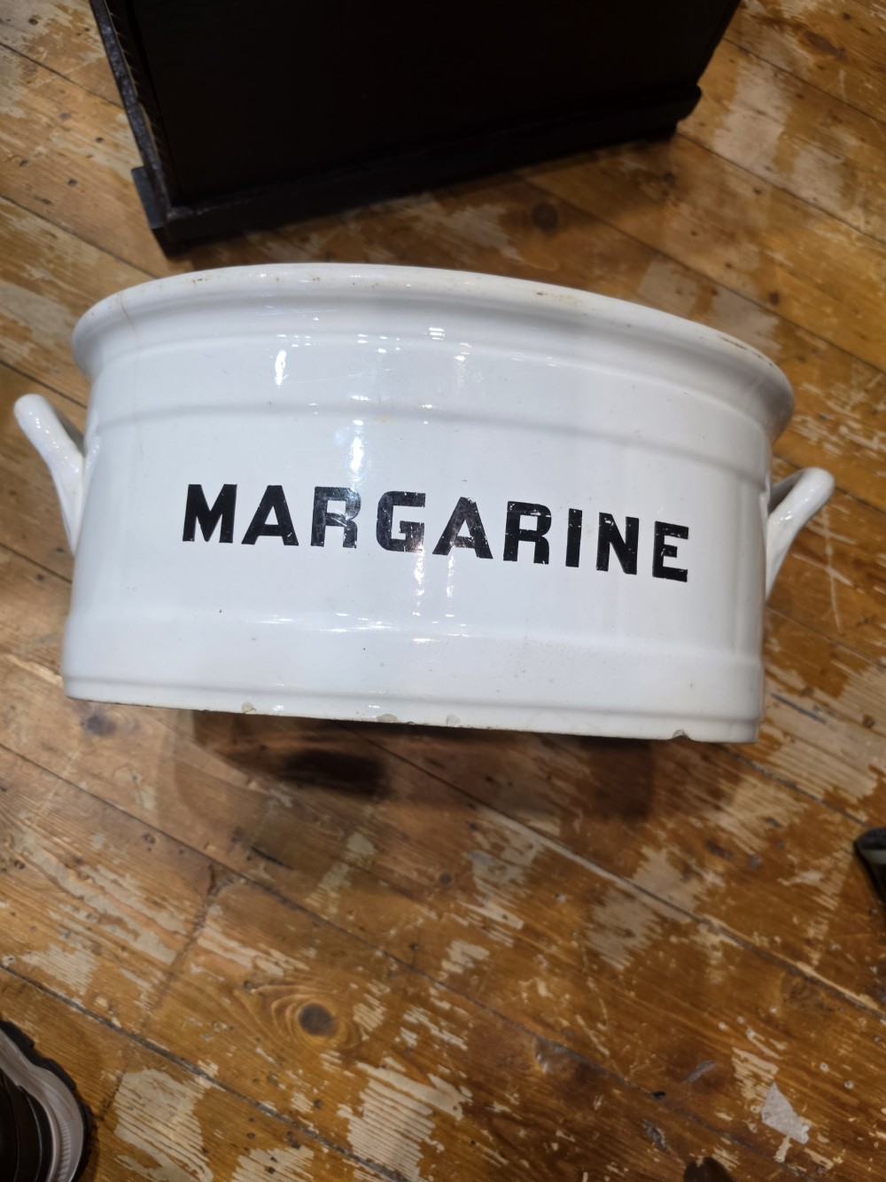 A white glazed ceramic oval tub with twin side handles, featuring bold black capital letters reading MARGARINE across the front. View VI