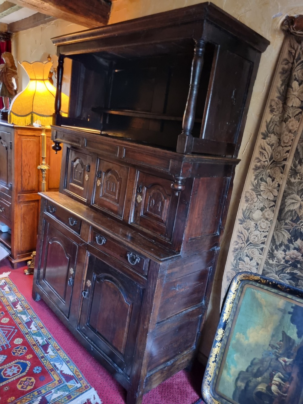 An eighteenth-century dark oak Welsh tridarn featuring a three-tiered structure with carved arched panels, turned pillars, and an inscribed date. View III