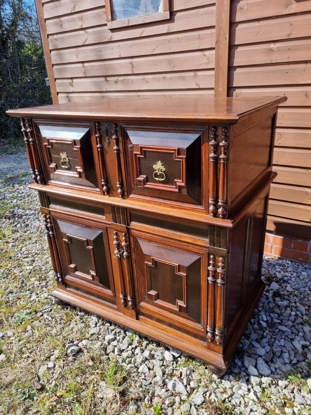 A mid 17th-century oak two-part chest featuring deep geometric recessed panels inlaid with dark wood, applied split spindles, and brass handles. View III