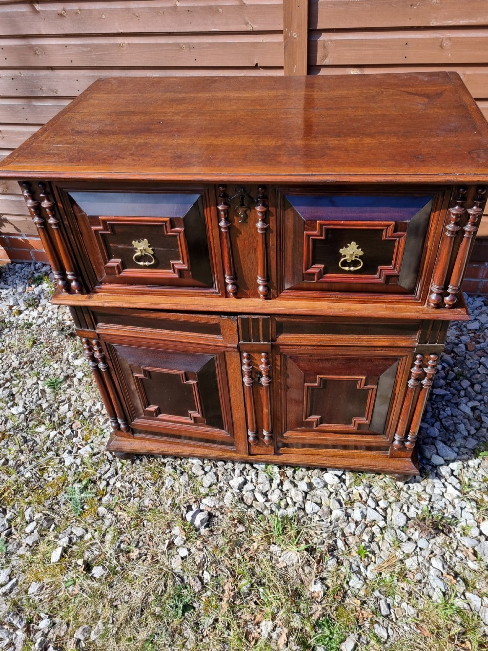 A mid 17th-century oak two-part chest featuring deep geometric recessed panels inlaid with dark wood, applied split spindles, and brass handles. View VI