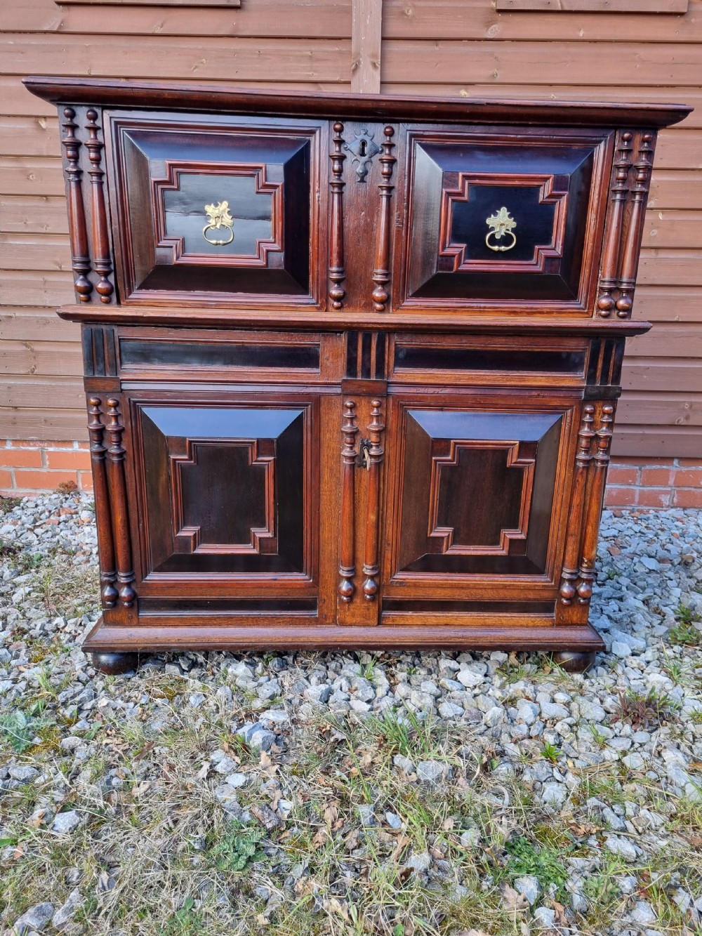 A mid 17th-century oak two-part chest featuring deep geometric recessed panels inlaid with dark wood, applied split spindles, and brass handles. View VII