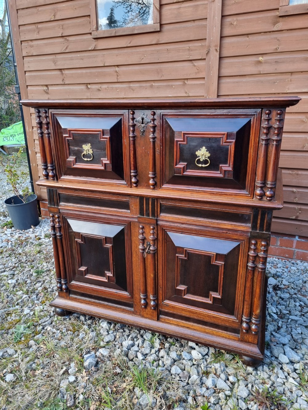 A mid 17th-century oak two-part chest featuring deep geometric recessed panels inlaid with dark wood, applied split spindles, and brass handles. View VIII
