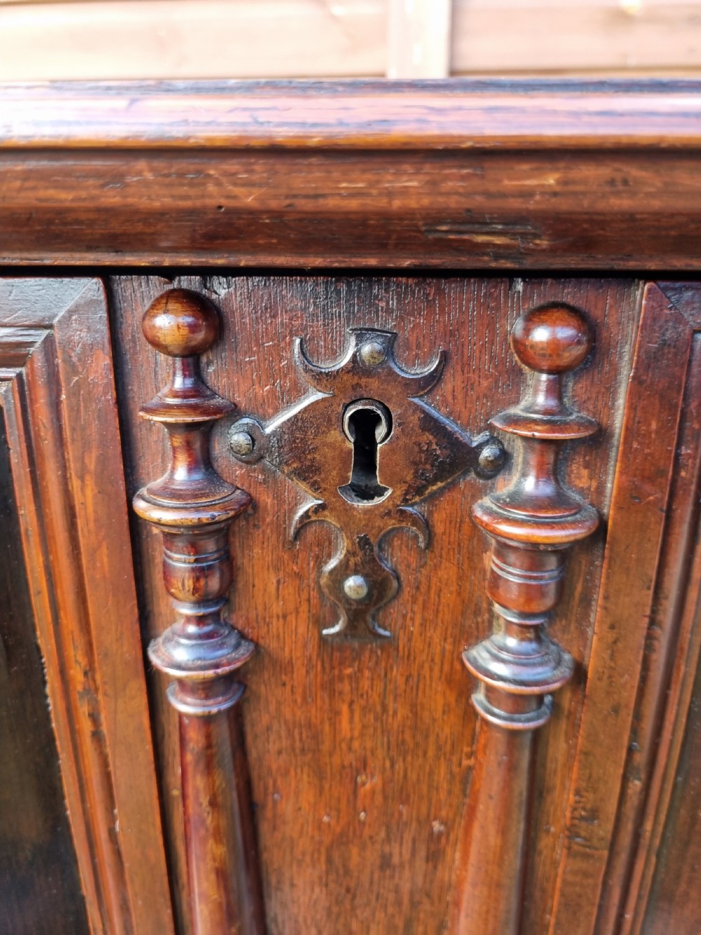 A mid 17th-century oak two-part chest featuring deep geometric recessed panels inlaid with dark wood, applied split spindles, and brass handles. View IX