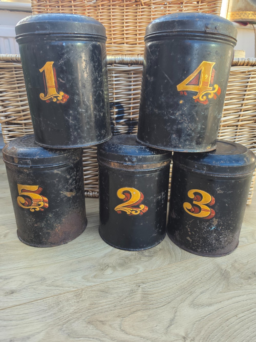 A set of five cylindrical black tin tea canisters numbered one through five with ornate gold and red painted numerals. View II