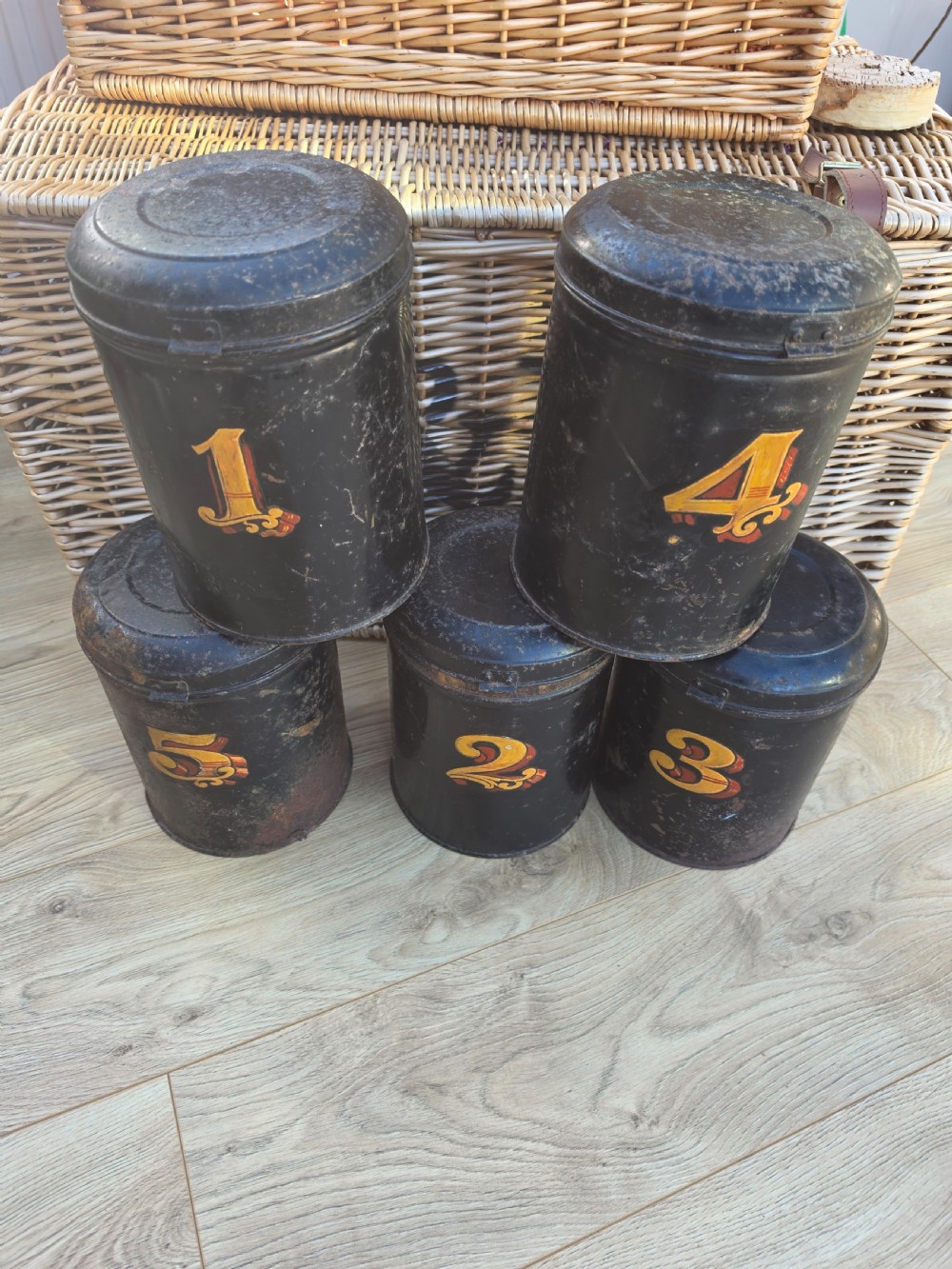 A set of five cylindrical black tin tea canisters numbered one through five with ornate gold and red painted numerals. View III