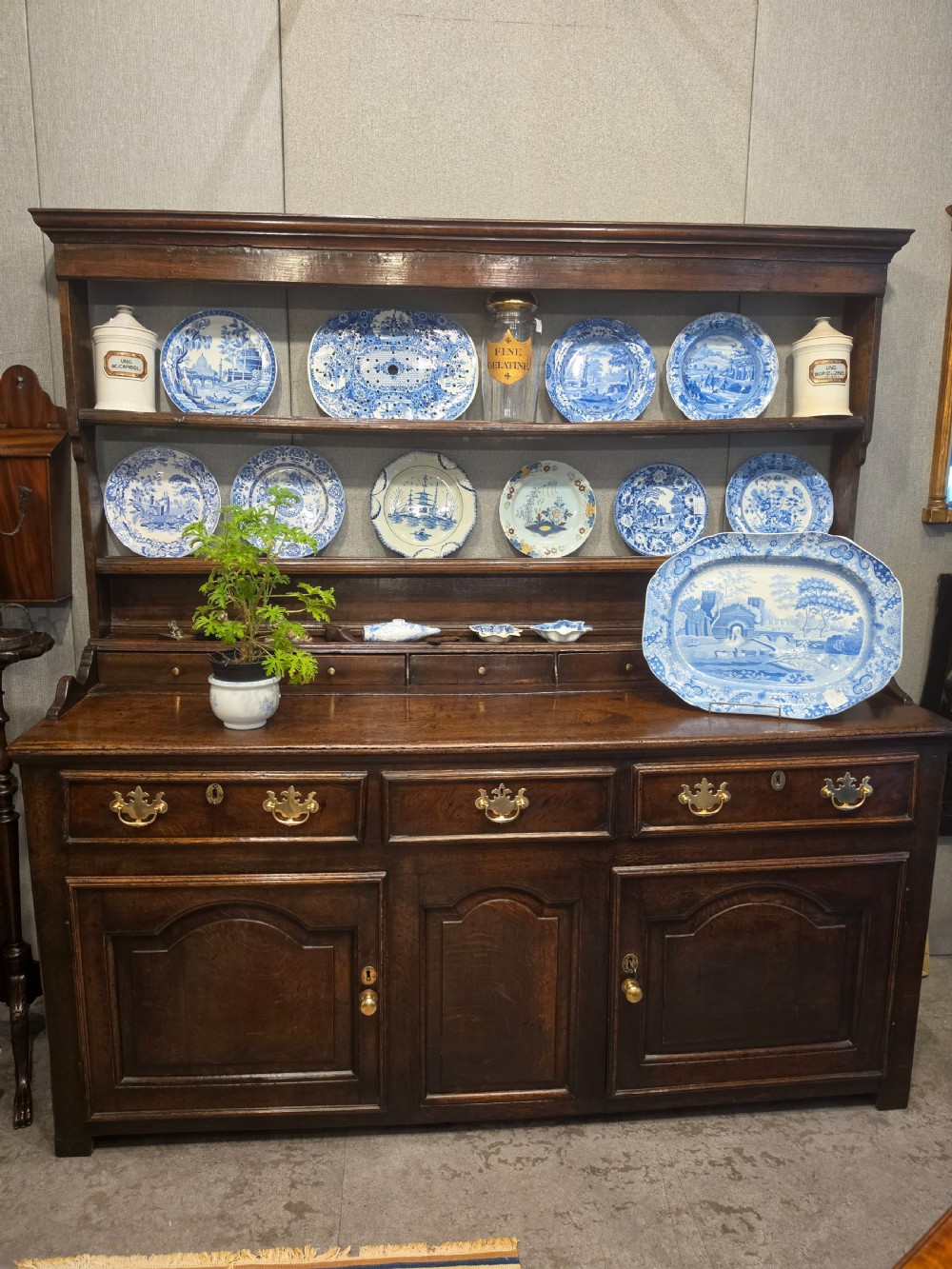 An 18th-century dark oak Welsh dresser featuring a three-tiered plate rack top above three drawers and three panelled cupboard doors with brass handles.