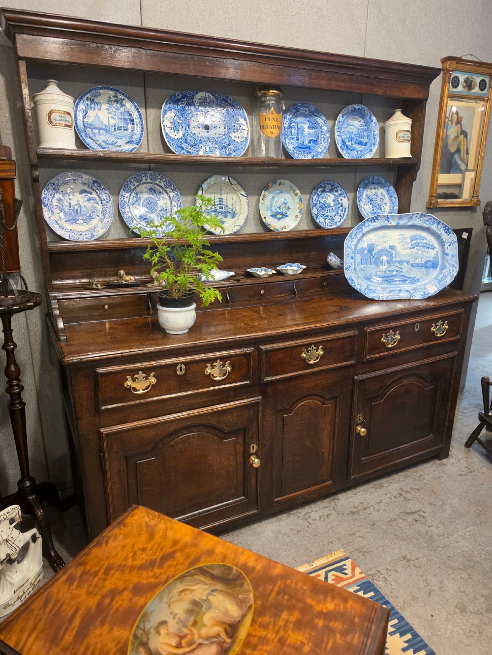 An 18th-century dark oak Welsh dresser featuring a three-tiered plate rack top above three drawers and three panelled cupboard doors with brass handles. View II