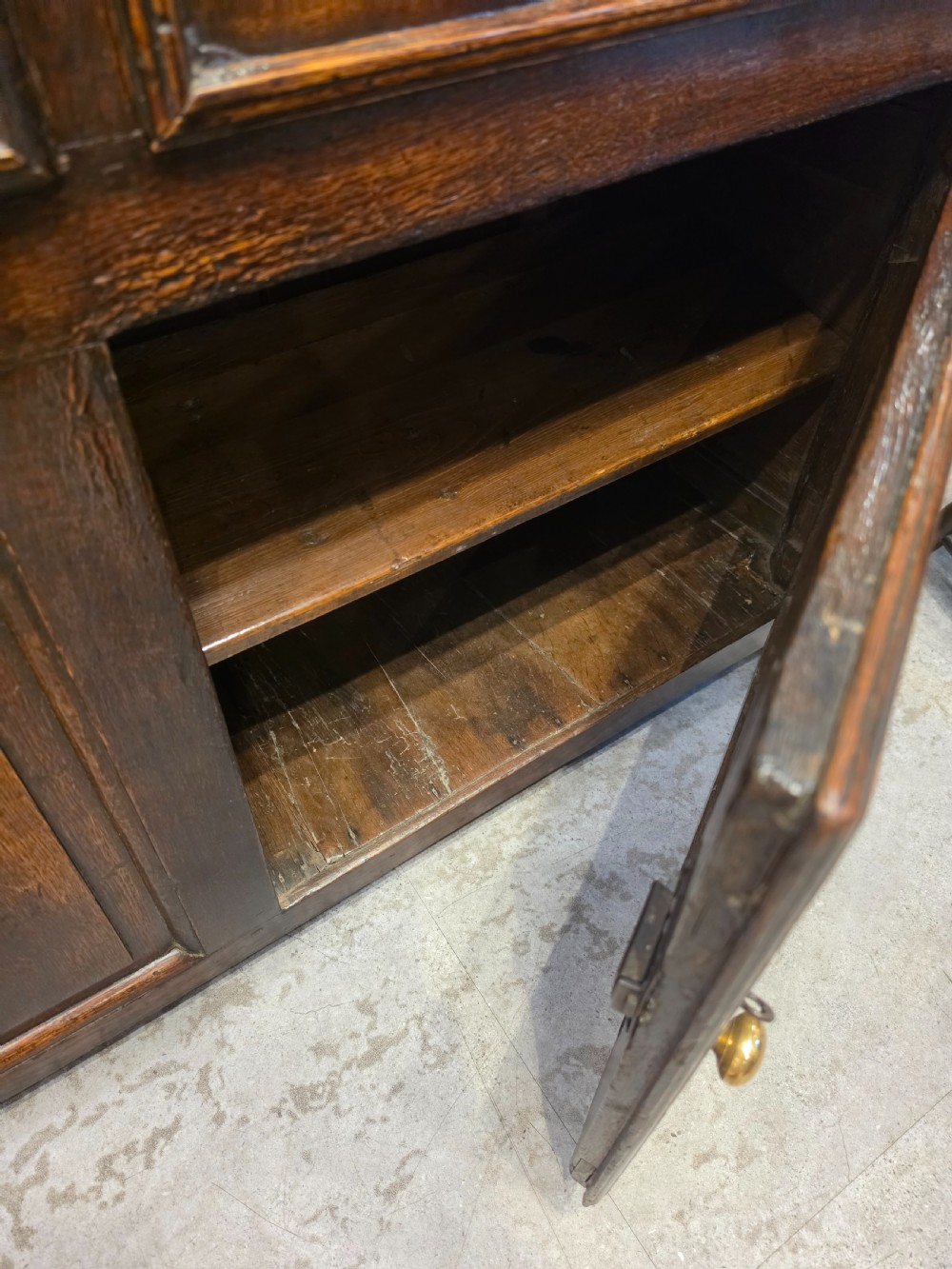 An 18th-century dark oak Welsh dresser featuring a three-tiered plate rack top above three drawers and three panelled cupboard doors with brass handles. View VI