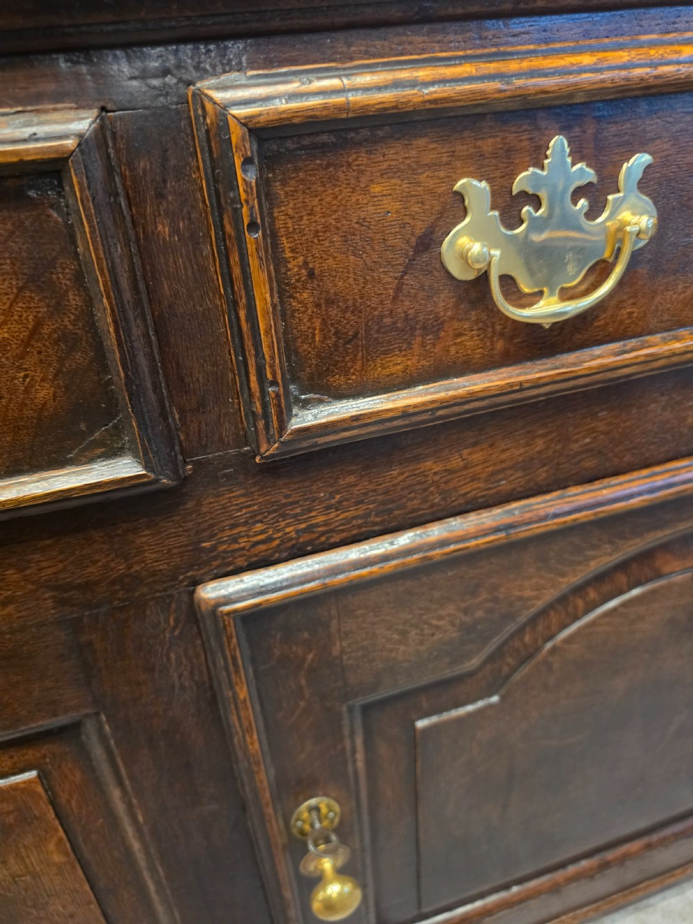 An 18th-century dark oak Welsh dresser featuring a three-tiered plate rack top above three drawers and three panelled cupboard doors with brass handles. View VII
