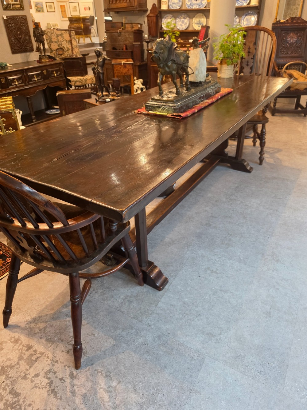 A large 19th-century dark elm refectory dining table featuring a solid planked top supported by a trestle stretcher base.