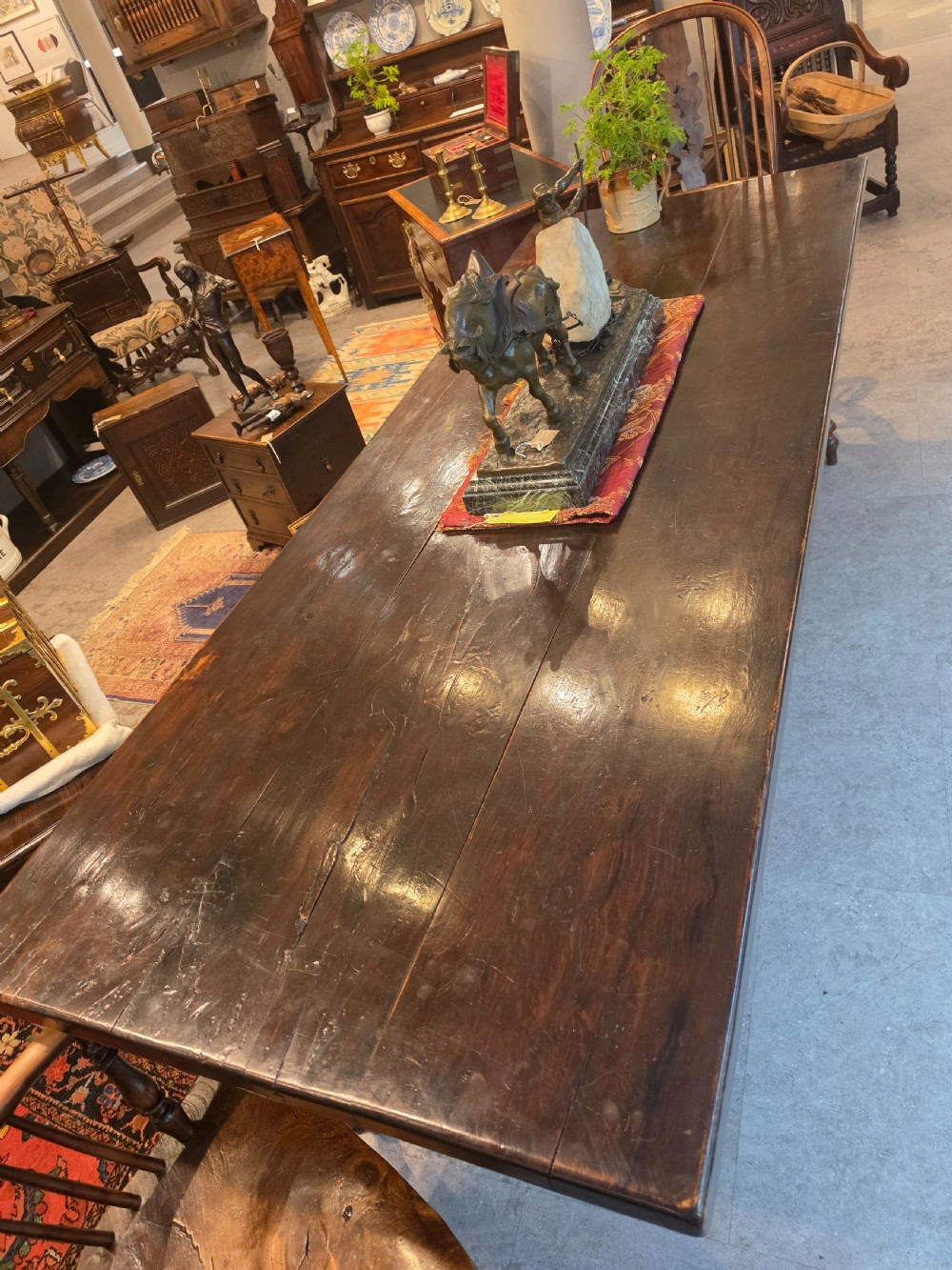 A large 19th-century dark elm refectory dining table featuring a solid planked top supported by a trestle stretcher base. View V