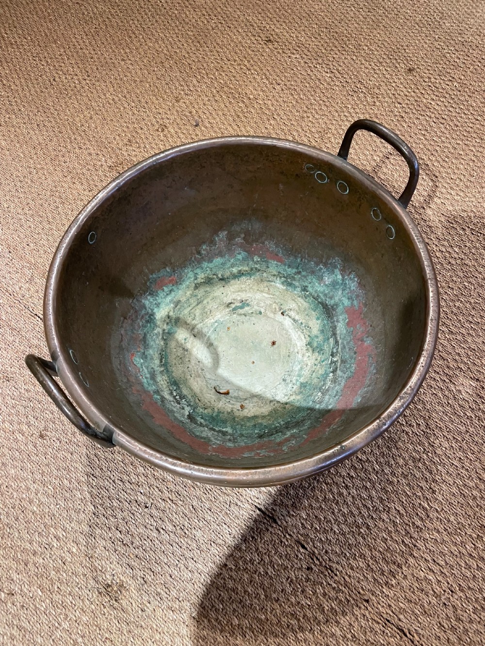 A round, hand-hammered antique copper pot with dual iron side handles and a weathered green patina on the interior base. View III