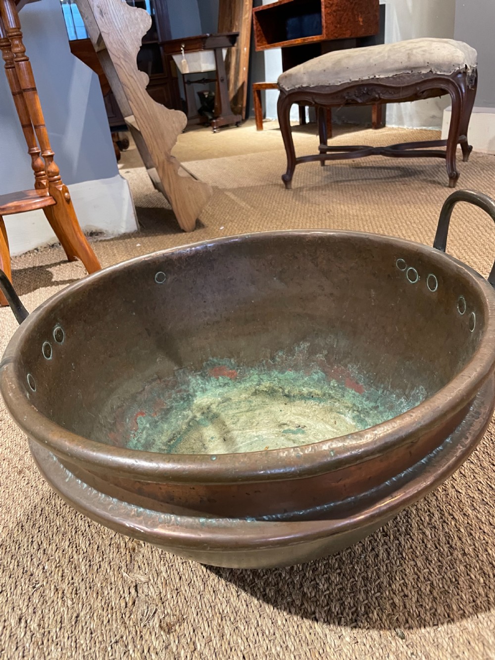A round, hand-hammered antique copper pot with dual iron side handles and a weathered green patina on the interior base. View IV