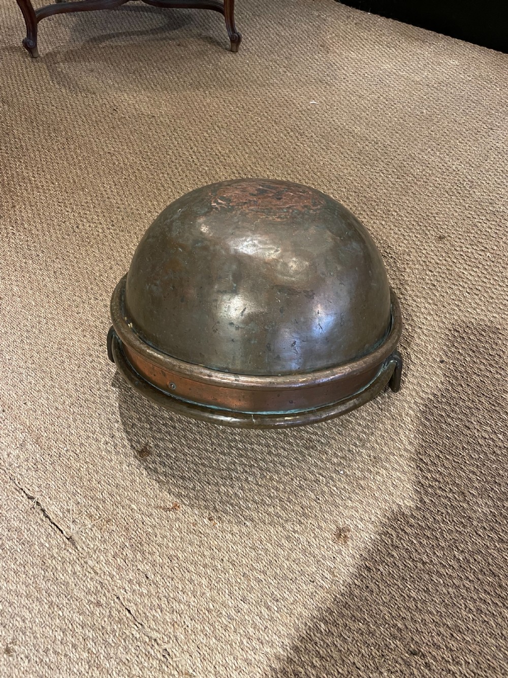 A round, hand-hammered antique copper pot with dual iron side handles and a weathered green patina on the interior base. View V