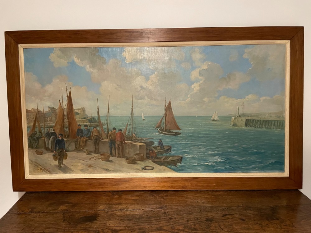 An early 20th-century oil painting on canvas depicting fishermen and sailing vessels at a stone harbour quay, set within a wide wooden frame.