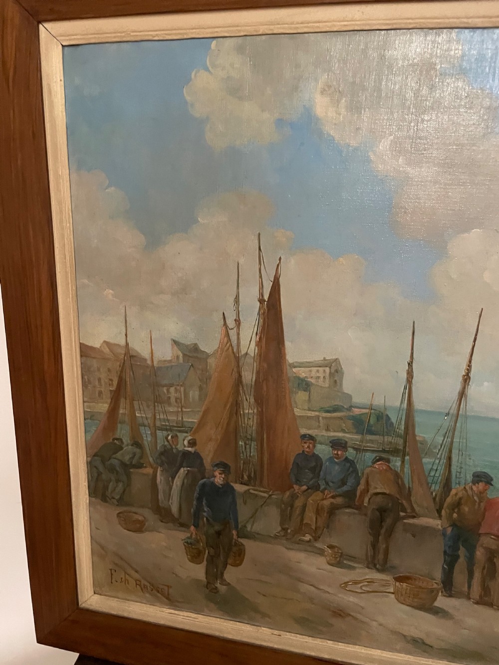 An early 20th-century oil painting on canvas depicting fishermen and sailing vessels at a stone harbour quay, set within a wide wooden frame. View IV