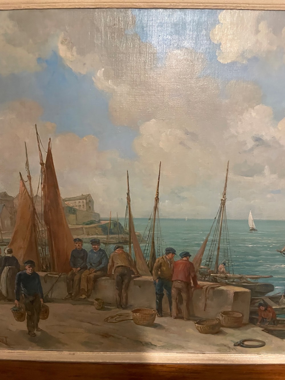 An early 20th-century oil painting on canvas depicting fishermen and sailing vessels at a stone harbour quay, set within a wide wooden frame. View VII