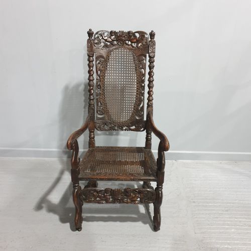 fig 1. A high-backed dark oak carver chair featuring an oval cane backrest, barley twist posts, hand-carved cresting, and a patterned seat cushion.