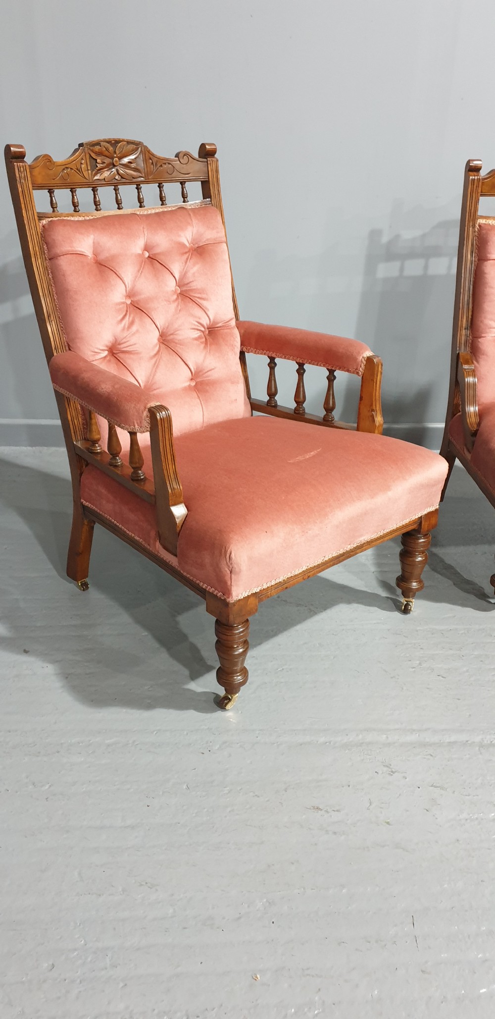 A pair of late Victorian carved oak chairs featuring button-tufted rose pink velvet upholstery and turned legs on brass castors. View II