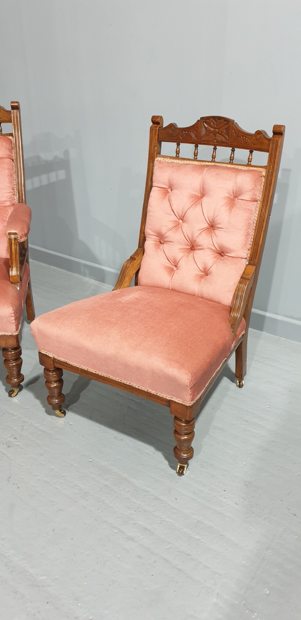 A pair of late Victorian carved oak chairs featuring button-tufted rose pink velvet upholstery and turned legs on brass castors. View III