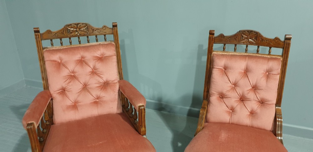 A pair of late Victorian carved oak chairs featuring button-tufted rose pink velvet upholstery and turned legs on brass castors. View V
