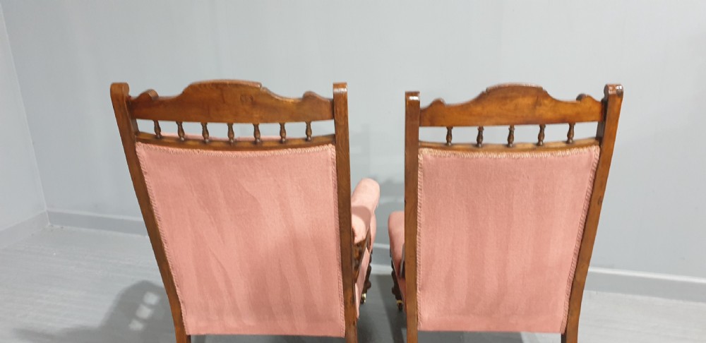 A pair of late Victorian carved oak chairs featuring button-tufted rose pink velvet upholstery and turned legs on brass castors. View VI