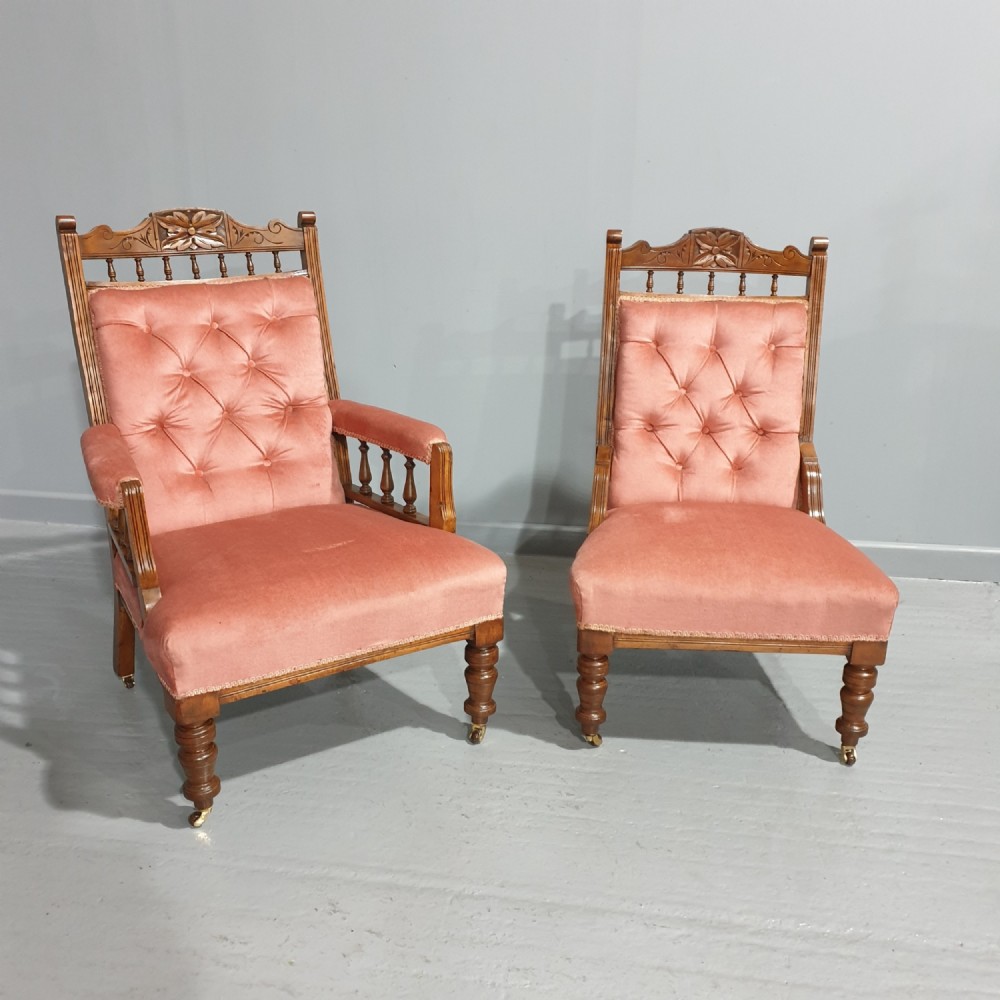 A pair of late Victorian carved oak chairs featuring button-tufted rose pink velvet upholstery and turned legs on brass castors.