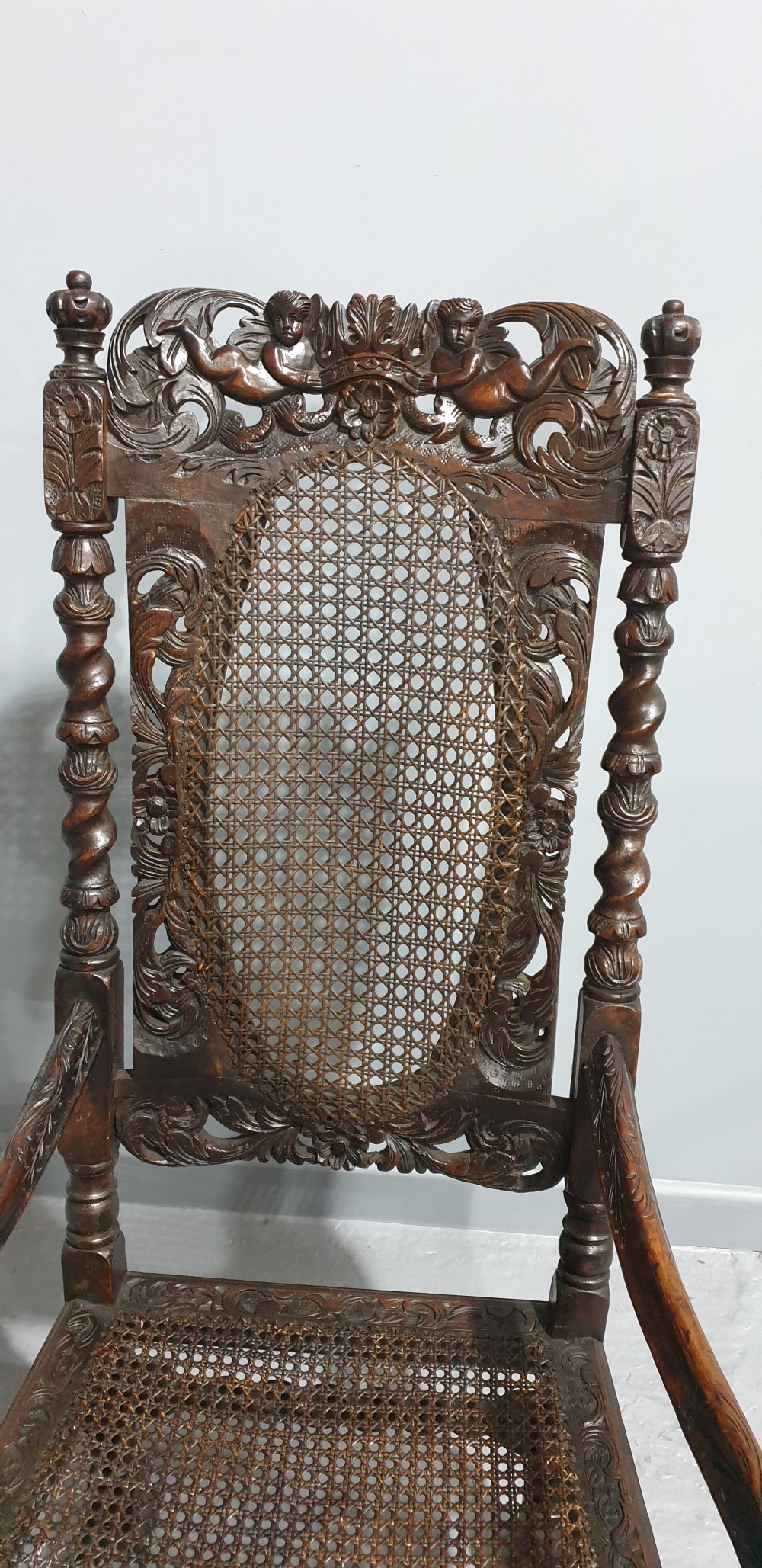 A high-backed dark oak carver chair featuring an oval cane backrest, barley twist posts, hand-carved cresting, and a patterned seat cushion. View III