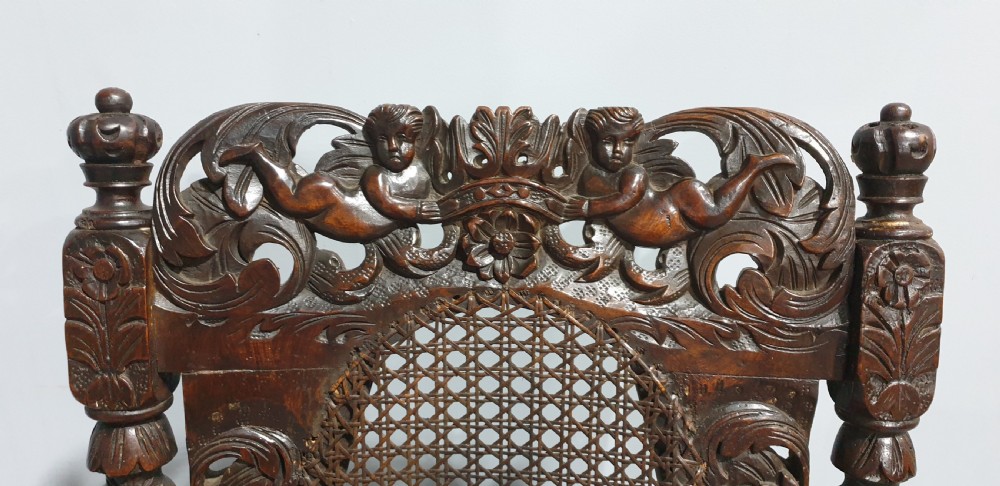 A high-backed dark oak carver chair featuring an oval cane backrest, barley twist posts, hand-carved cresting, and a patterned seat cushion. View IV
