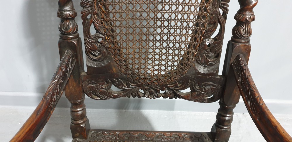 A high-backed dark oak carver chair featuring an oval cane backrest, barley twist posts, hand-carved cresting, and a patterned seat cushion. View V