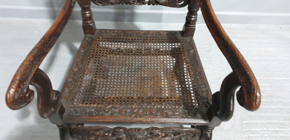 A high-backed dark oak carver chair featuring an oval cane backrest, barley twist posts, hand-carved cresting, and a patterned seat cushion. View VI