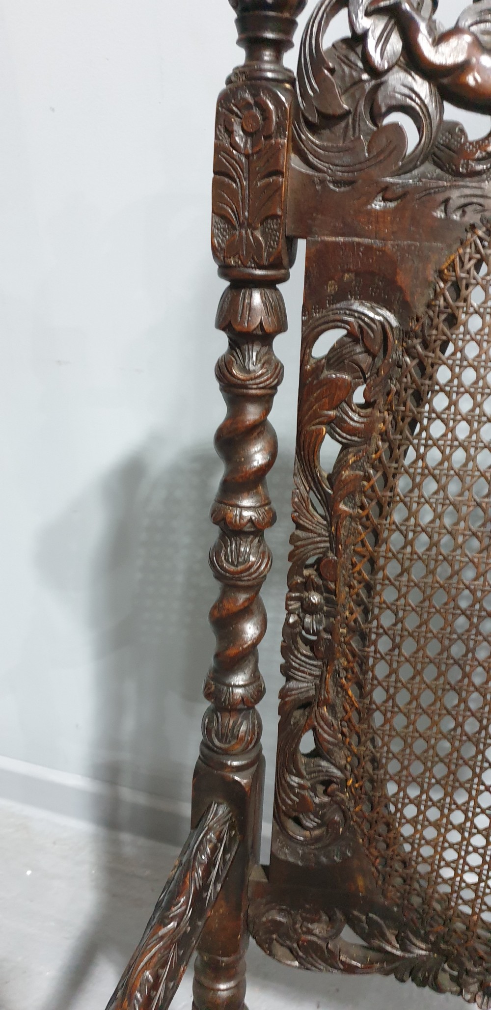 A high-backed dark oak carver chair featuring an oval cane backrest, barley twist posts, hand-carved cresting, and a patterned seat cushion. View VII