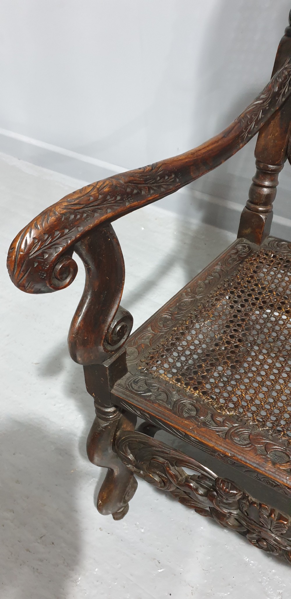 A high-backed dark oak carver chair featuring an oval cane backrest, barley twist posts, hand-carved cresting, and a patterned seat cushion. View IX
